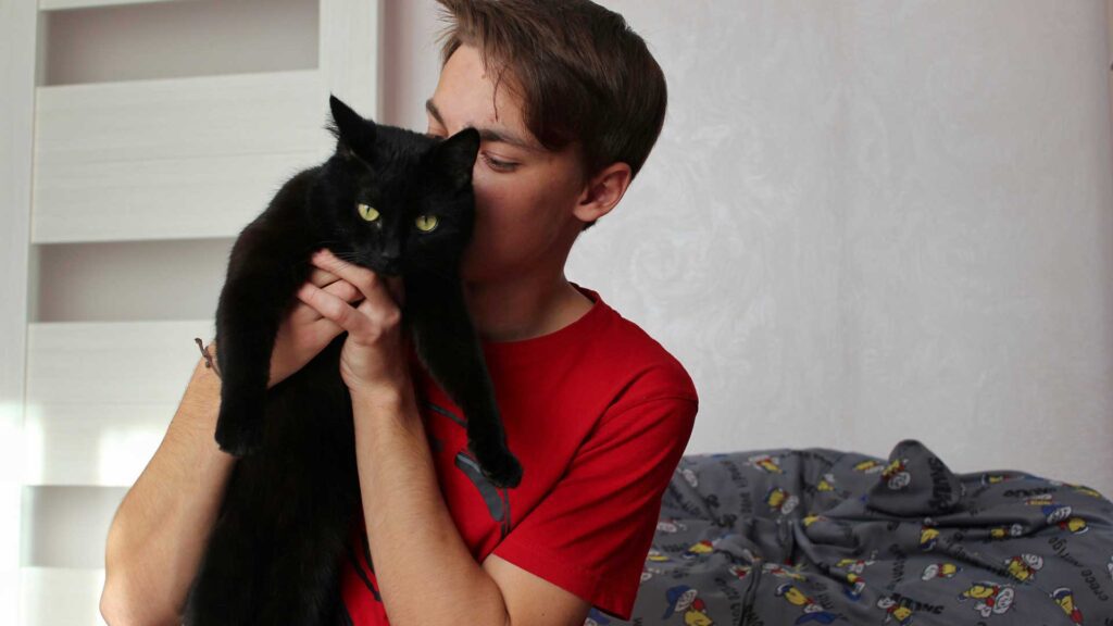 man holding cat while sitting against wall at home.